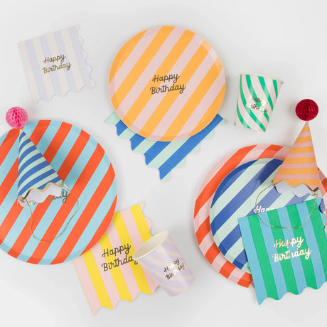 An assortment of colorful striped birthday party tableware, including plates, cups, napkins, and hats.