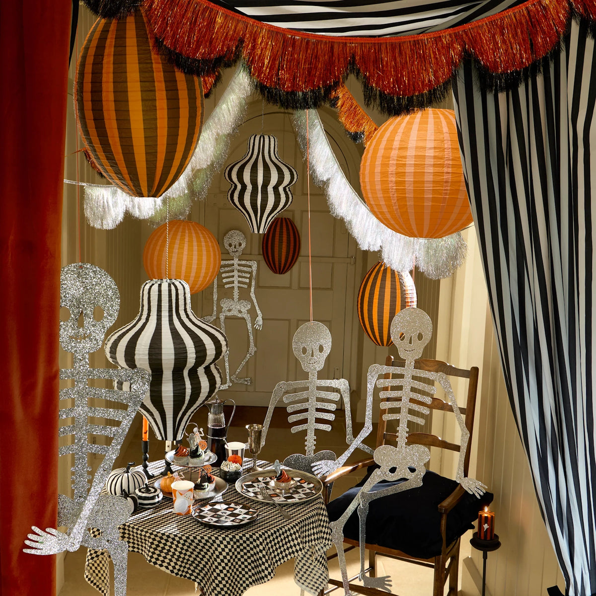 Festive Halloween room decorated with striped paper lanterns, glittery skeletons, and table settings.