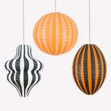 Three striped hanging paper lanterns in distinct shapes, colored black, orange, peach, and white.