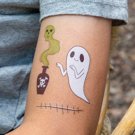 Child's arm with temporary tattoos of a ghost, a poison bottle with green smoke, and stitches.