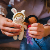 Child hands holding a small plush doll in a bunny suit alongside a tiny purple mermaid doll.