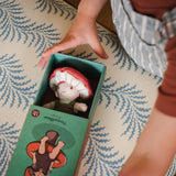 Child opening a green illustrated box to reveal a small toadstool plush doll inside.