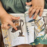 Toddler's hands pointing to a deer illustration in a soft cloth book.