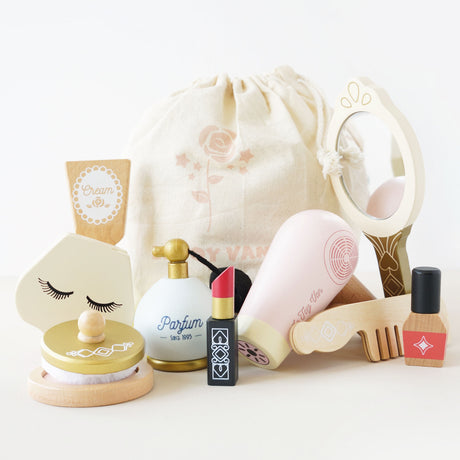 Wooden beauty play set with mirror, hair dryer, perfume, and makeup arranged in front of a cloth bag.