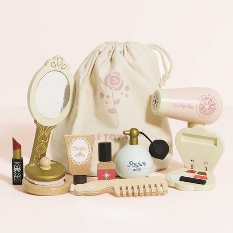 Wooden toy beauty kit with hand mirror, hairdryer, makeup, and comb in front of a drawstring bag.