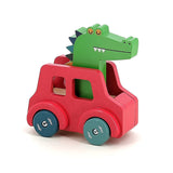Vilac wooden toy crocodile driving a red car with blue wheels, side view isolated on a white background.