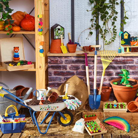 Toy gardening tools, wheelbarrow, and wooden play food set up in a garden themed display.