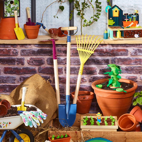 Colorful wooden kids' garden tool set with shovel, rake, and wheelbarrow displayed against a rustic brick wall.