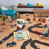 Wooden toy cars, blue ride-on car, and a toy moving truck on a play road track on a playroom floor.