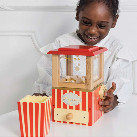 Young girl smiling as she plays with a red-striped vintage wooden toy popcorn machine.