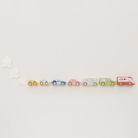 Seven vintage-style wooden toy cars lined up in a row with white felt exhaust clouds on a beige background.