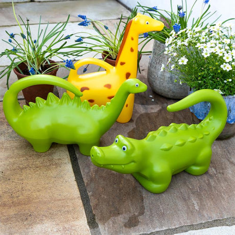 Green dinosaur, yellow giraffe, and lime crocodile animal-shaped watering cans on a stone patio with potted garden flowers.