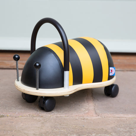 Plush bumblebee Wheely Bug ride-on toy with wheels and black handle on a stone patio.