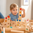 A young child builds a tower with wooden blocks featuring colorful transparent windows. The setting is bright and cheerful, promoting creativity and concentration.