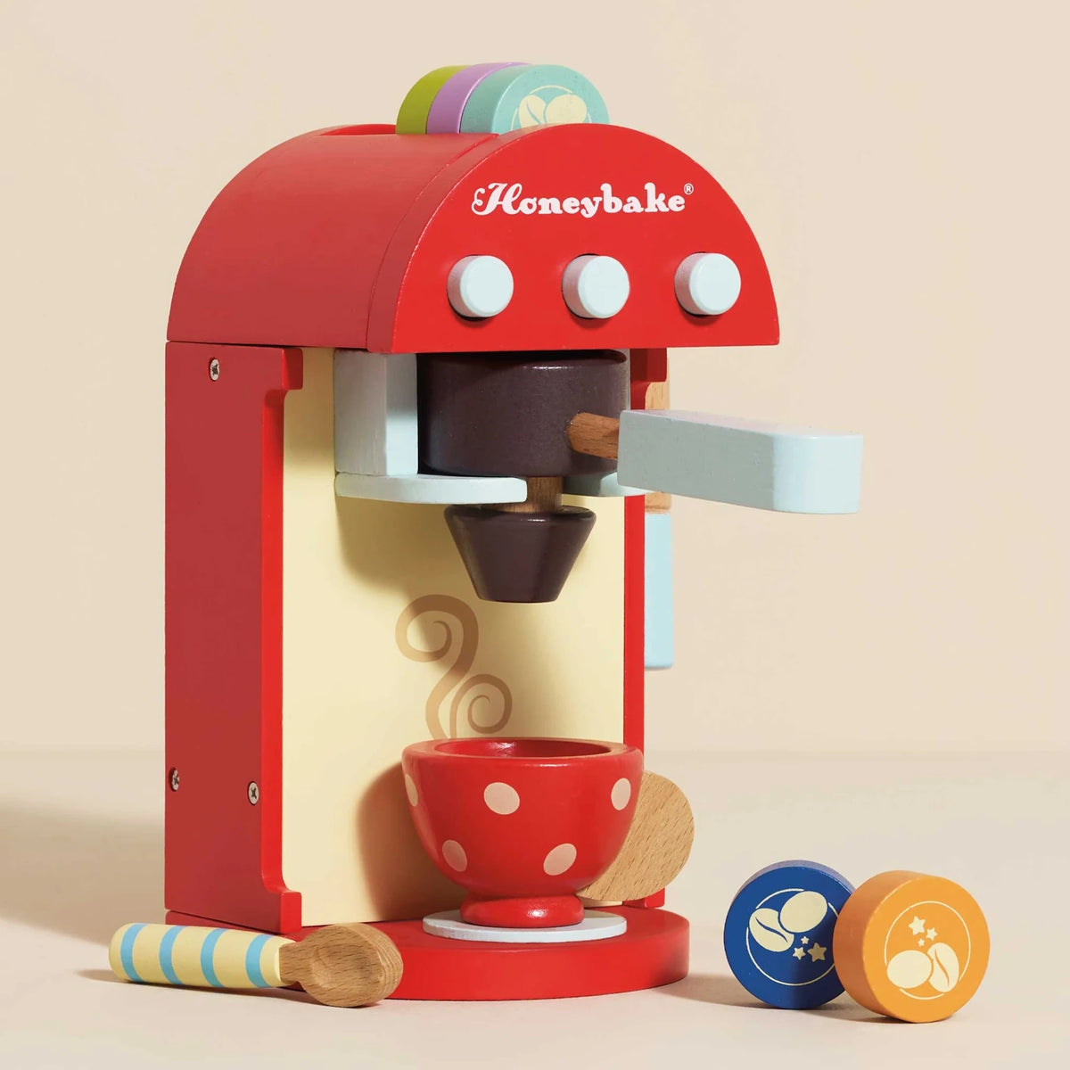 A colorful wooden toy coffee machine with a polka-dot cup, spoon, and coffee pods.