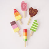 Flat lay view of six wooden toy ice lollies/popsicles arranged on a light background.