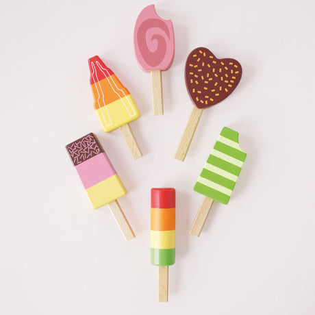 Flat lay view of six wooden toy ice lollies/popsicles arranged on a light background.
