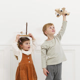 Young girl holding a wooden toy boat on her head next to a boy raising a wooden toy plane.