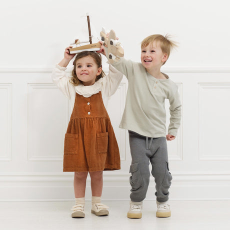 Two children happily playing together holding a wooden toy sailboat and a wooden toy plane.