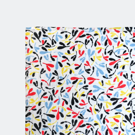 Fabric with a playful, colorful pattern of abstract leaves in red, yellow, blue, and black on a white background, conveying a lively, cheerful tone.